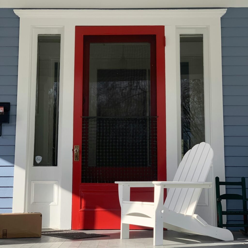 Front porch with a red door and Adirondack chair providing a welcoming vibe.